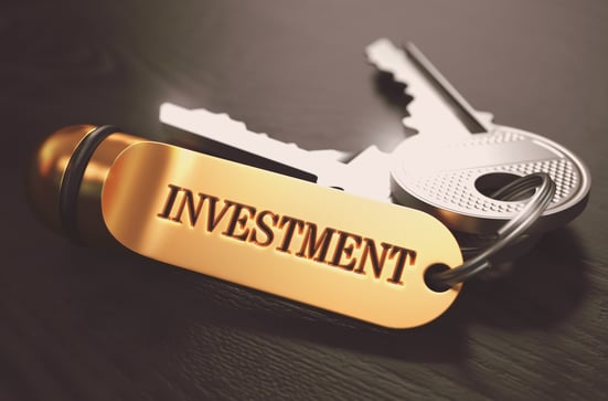 Keys with Word Investment on Golden Label over Black Wooden Background. Closeup View